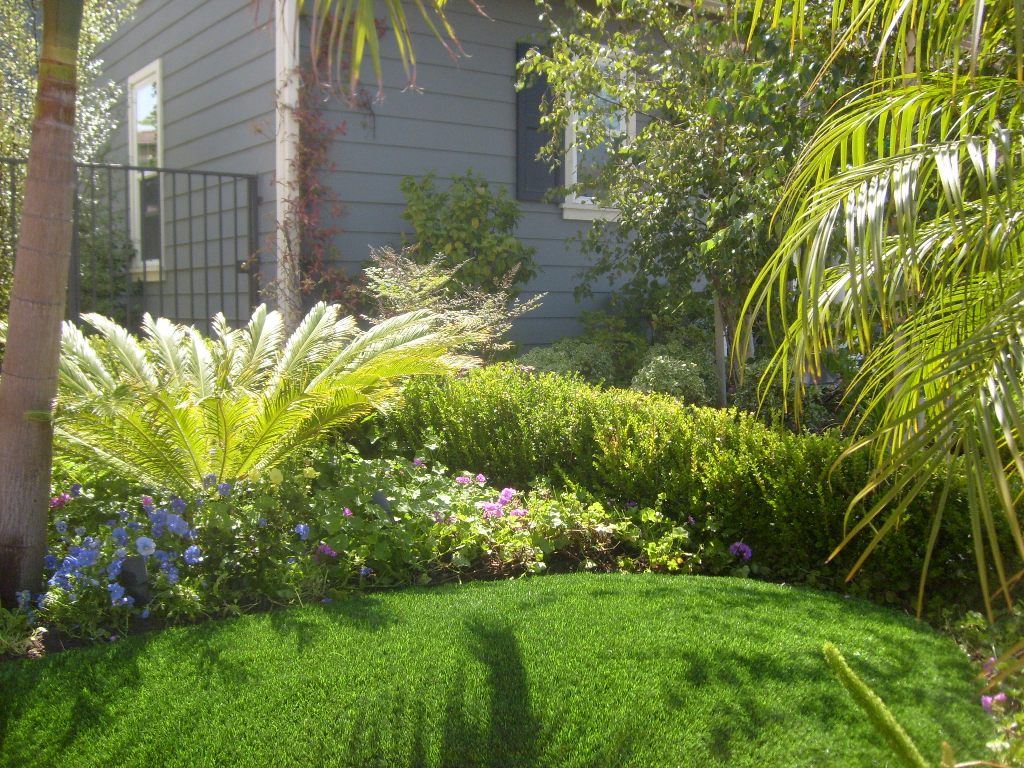 Synthetic grass yard lined by a colorful garden